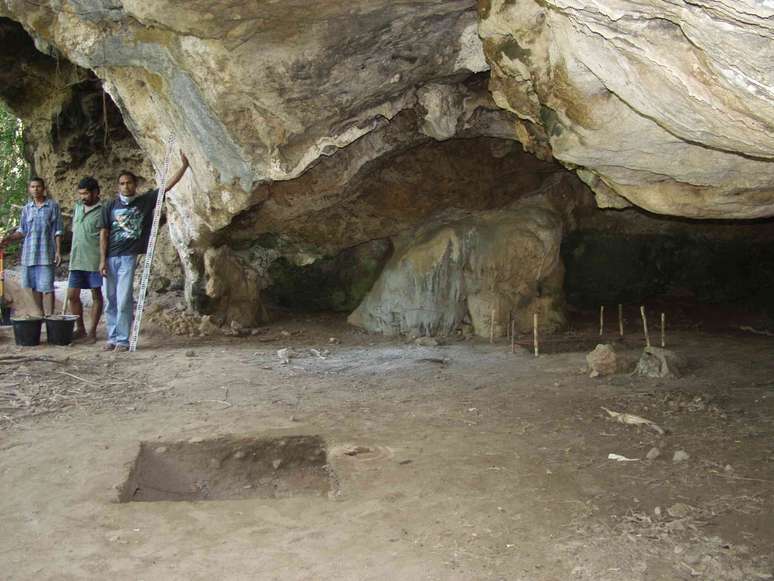 Tr&ecirc;s pessoas est&atilde;o ao lado de uma caverna com piso de terra