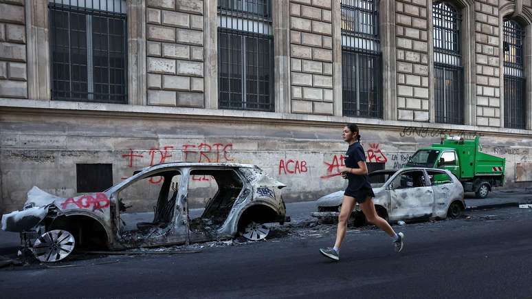 Uma mulher faz exerc&iacute;cios perto de ve&iacute;culos carbonizados em Paris, perto da Place de la R&eacute;publique