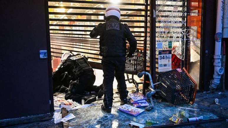 Agentes da pol&iacute;cia det&ecirc;m uma pessoa em uma loja em Paris que foi saqueada durante os tumultos de domingo