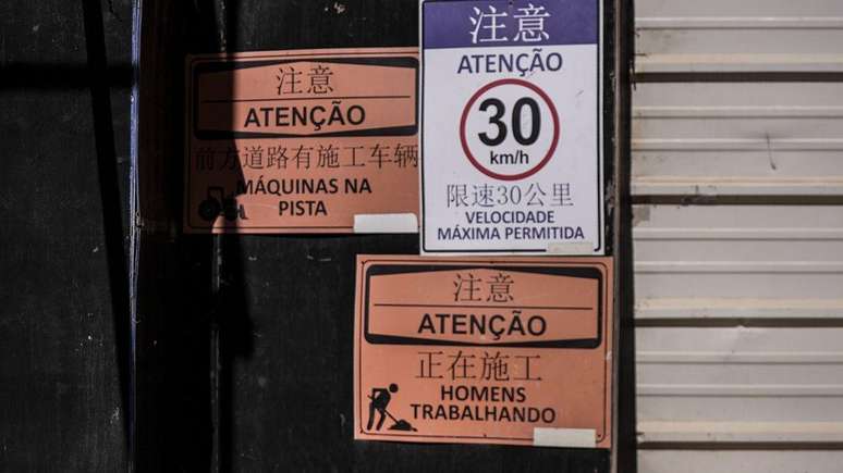 Entrada do canteiro de obras do alojamento da BYD com placas em portugu&ecirc;s e mandarim com os dizeres "homens trabalhando", "m&aacute;quinas na pista" e "velocidade m&aacute;xima permitida 30km/h"