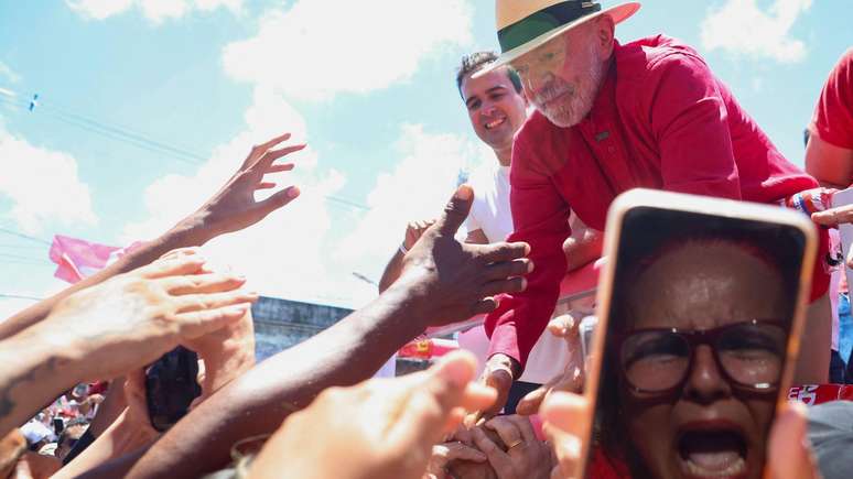 Lula fala com apoiadores em ato de campanha. Uma mulher grita enquanto segura seu celular em frente a Lula