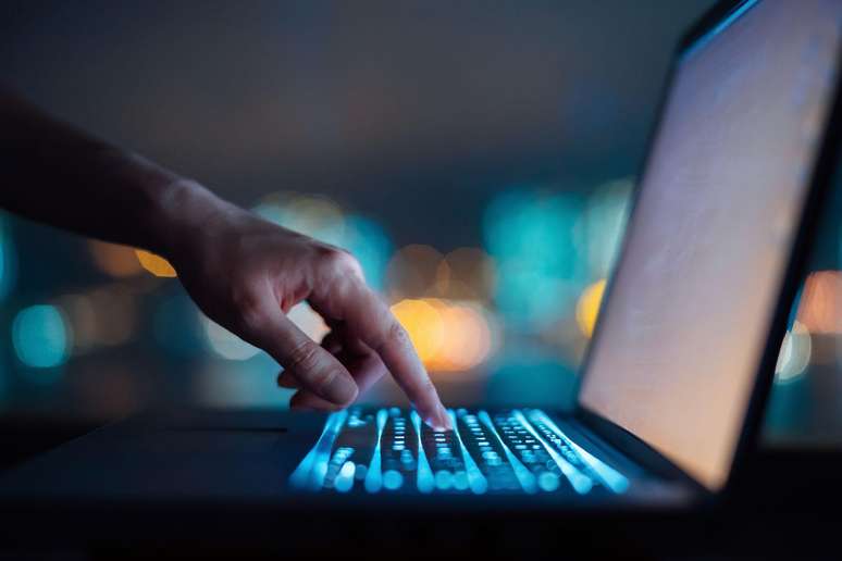 Dedo mexendo em laptop, em ambiente escuro