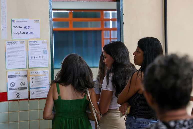 Eleitores fazem fila e olham cartaz com informa&ccedil;&otilde;es sobre se&ccedil;&atilde;o eleitoral