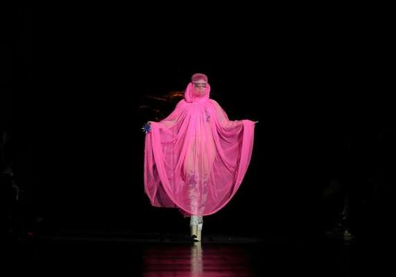 Gaga acaparó todas las miradas en la primera jornada de la Semana de la Moda de Londres. La cantante, gracias a sus excéntricos looks, dejó en segundo plano a los diseñadores de la pasarela londinense. Gaga desfiló para el diseñador Philip Treacy con una capa rosa flúor que cubría todo su cuerpo. Al ser semitransparente, se pudo ver que debajo llevaba puesto un ajustado mono color carne flores estampadas. Minutos antes del desfile, la cantante lució un vestido de terciopelo verde y leggins doradas. Pero todas las miradas se desviaban a su cabeza, en la que llevaba una corona de flores que le cubría toda la cara. También se la vio con unas enormes orejas de Minnie Mouse con incrustaciones de pedrería que hacían juego con su camisa, encima de la que llevaba una chaqueta blanca decorada con perlas. Esto no fue todo, Lady Gaga sorprendió al público londinense con un último cambio de vestuario: un modelo turbante que incluía pieles colgantes.