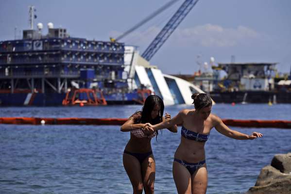 15 de julho - Banhistas aproveitam dia de calor em frente ao navio Costa Concordia, que está encalhado na costa da Ilha de Giglio. Equipes de remoção trabalham contra o tempo para endireitar e remover o navio que está se comprimindo contra o granito do fundo do mar. Segundo as autoridades, o casco do cruzeiro já se comprimiu 3 metros desde que colidiu com rochas locais no dia 13 de janeiro de 2012. O acidente custou a vida de 32 pessoas