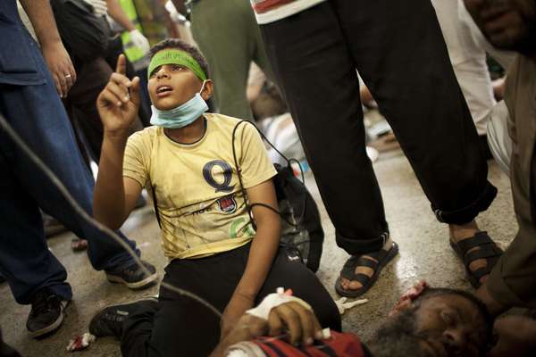 Menino egípcio ora de joelhos ao lado de seu pai, um simpatizante de Mursi que foi baleado durante confronto com as forças de segurança em Cidade Nasr. nos arredores do Cairo
