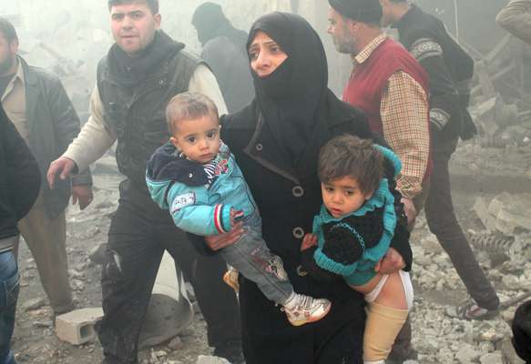 Moradora de Aleppo carrega crianças instantes após ataques aéreos à cidade no dia 15 de dezembro