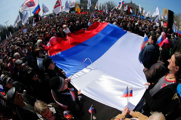 Ativistas seguram uma enorme bandeira russa em frente ao prédio da administração regional em Donetsk, Ucrânia, neste domingo. Um grupo de pessoas invadiu o edifício do governo provincial: uma inscrição na bandeira russa colocada na fachada do local dizia: "República Donetsk"
