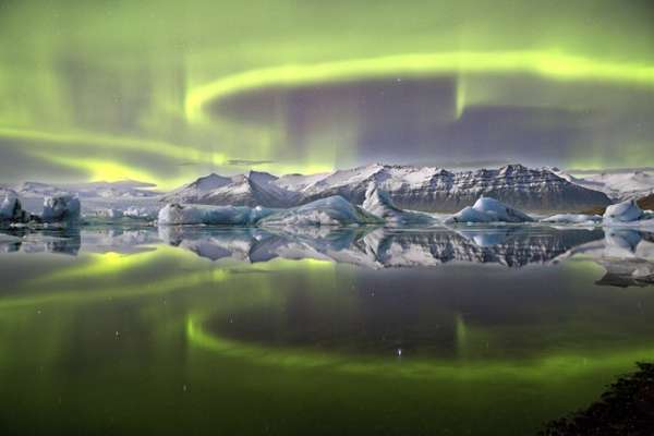 A aurora verde e vívida que cruza o céu noturno islandês é refletida na lagoa glacial de Vatnajökull, no Parque Nacional Jökulsarlon. A imagem foi tirada pelo fotógrafo britânico James Woodend, que ganhou o prêmio de Fotógrafo da Astronomia de 2014.