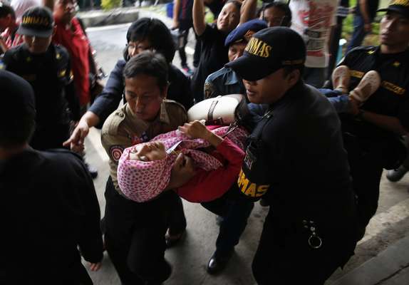 Seguranças do aeroporto de Surubaia (Indonésia) carregam parente desmaiada de um dos passageiros que estava a bordo do avião da AirAsia