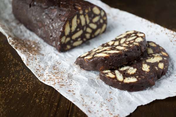 Salame de Chocolate*Receita do site Lo Spicchio D’aglio Ingredientes 100 g de manteiga 250 g de biscoitos tipo maisena 2 ovos 100 g de açúcar 1 colher de sopa de rum 50 g de cacau em pó sem açúcar Açúcar de confeiteiro para polvilhar (opcional) Modo de preparo Coloque os biscoitos maisena dentro de um pano de prato limpo e amasse com um batedor de carne até ficarem grosseiramente despedaçados (ou use um processador, mas não deixe muito tempo, os pedaços devem ficar pequenos, mas não moídos). Derreta a manteiga em uma panela com cuidado para não deixá-la aquecer, deve apenas se dissolver. Em uma tigela bata os ovos, que devem estar em temperatura ambiente, com um batedor e adicione o açúcar. Misture para obter uma mistura homogênea, em seguida, adicione o rum e incorpore. Finalmente, adicione a manteiga derretida. Quando obtiver uma pasta macia e suave, acrescente o cacau em pó e misture bem com uma colher de pau. Por fim, adicione os biscoitos e misture. Coloque a massa sobre uma folha de papel manteiga e enrole em formato de salame, cuidado para não deixar muito fino. Polvilhe o salame com o açúcar em pó e, em seguida, envolva o doce em uma folha de papel alumínio ou filme plástico. Coloque-o no congelador por pelo menos 2 horas. Se o doce não for consumido todo na hora, você pode sempre guardar o restante no congelador para mantê-lo durinho.