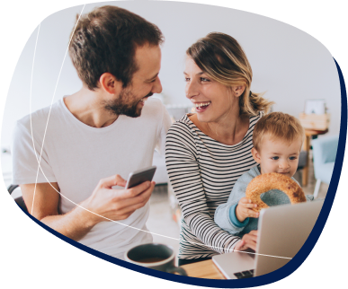 Casal com um bebe no colo sorrindo e mexendo no celular e no computador