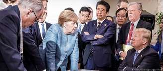 Angela Merkel (c., de pé) diante de Donald Trump na mesa de negociações do G7