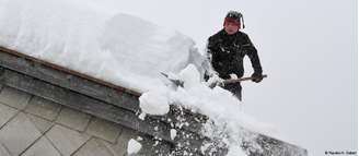 Homem remove camada de neve do telhado de sua casa em Inzell, na Alta Baviera