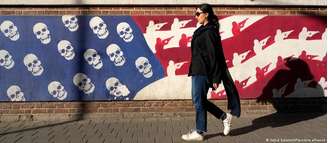 Em 2024, mulher em Teerã passava por mural representando bandeira dos Estados Unidos com caveiras no lugar de estrelas, e soldados armados enfileirados nas listras vermelha e branca