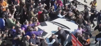 Um homem aparece tentando subir no capô do veículo em que Milei estava 