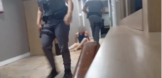 A mulher aparece sentada encostada na parede ao lado de uma poça de sangue