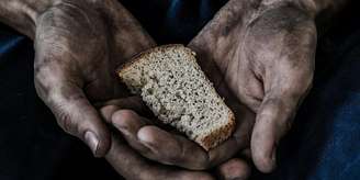 Imagem enquadra duas mãos que seguram um pedaço de pão