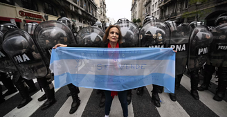 Manifestante segura bandeira argentina na frente de policiais nos arredores do Congresso Nacional em Buenos Aires.
