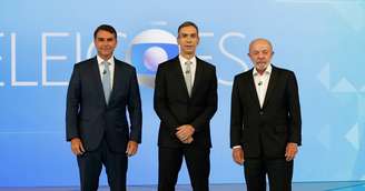 O mediador César Tralli com os candidatos Flávio Bolsonaro (PL) e Lula (PT): debate de 2º turno na Globo foi o ponto alto de audiência na cobertura eleitoral de 2026