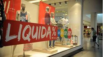 Imagem mostra vitrine de loja com placa de liquidação. 
