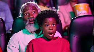 Idoso e jovem olhando assustados para a tela em uma sala de cinema