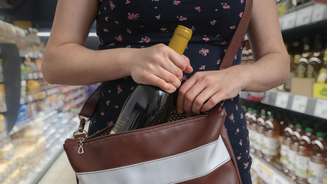 Mulher colocando garrafa em bolsa dentro de loja