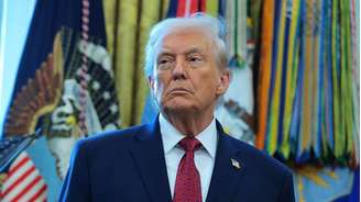 Donald Trump com olhar sério, em frente a bandeiras