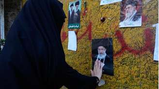 Mulher presta homenagem diante de um retrato de Ali Khamenei em Teerã; funeral do ex-líder supremo mobiliza multidões e é tratado pelo regime iraniano como uma demonstração de força política.