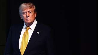 Trump usando um terno com uma gravata amarela. O fundo é preto.