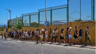 Migrantes são conduzidos por soldados espanhóis em direção à fronteira com Marrocos após entrarem em Ceuta; Espanha afirma ter devolvido a maioria das pessoas que cruzaram ilegalmente para o enclave.