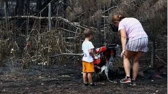 Uma mãe e seu filho inspecionam os arredores de sua casa em Le Porge, na segunda-feira, após ela ter sido destruída por um incêndio florestal