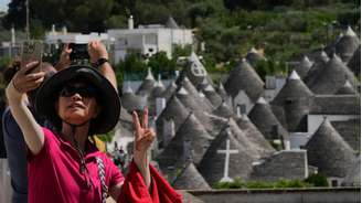 Uma turista faz uma selfie tendo como pano de fundo as habitações de pedra seca com telhados cônicos chamadas “trulli”, em Alberobello, na região sul da Puglia, em 24 de junho de 2026.