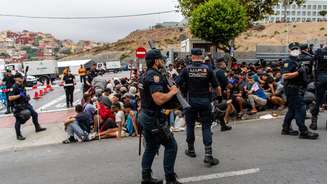 Policiais vigiam grupo de migrantes que aguardam entrada no Centro de Recepção de Loma Colmenar. (01/09/2026)