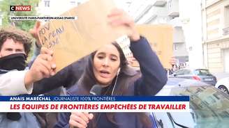 A repórter Anaïs Maréchal se desvencilha dos cartazes colocados à sua frente para tentar trabalhar