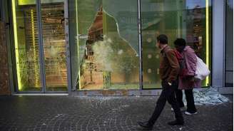 Pessoas passam, na manha de 19 de outubro de 2026, diante de vitrine de loja vandalizada durante protestos no centro de Paris, em 17 de outubro de 2026.