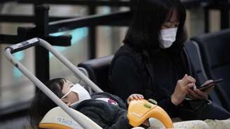 Mulher e criança com máscaras no aeroporto internacional de Tóquio; fábrica de máscaras está trabalhando extra para atender demanda