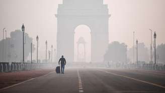 Um homem com uma mala caminha em direção ao Portão da Índia em Nova Déli envolto em poluição