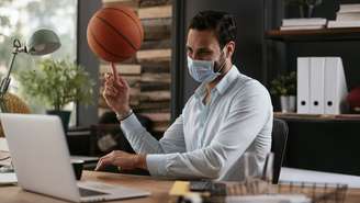 Homem trabalhando no laptop enquanto gira bola de basquete