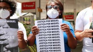 Imagem mostra a avó da criança segurando um cartaz com o letreiro "Justiça Por Miguel"