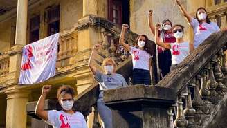 Imagem mostra seis mulheres na escada que dá acesso ao Centro de Referência Soledad Barret com os punhos fechados, em alusão ao símbolo da luta feminista