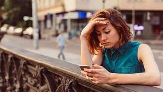 mulher branca com mão na testa e olhando o celular