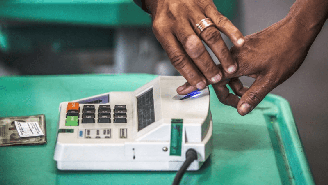 Imagem mostra mãos negras fazendo identificação biométrica para votar.