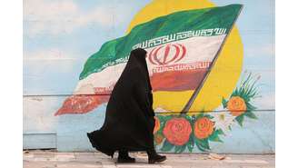 Mulher caminha em Terrã ante grafite com bandeira do Irã 