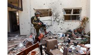 Um soldado israelense passa por cima de pertences pessoais perto de uma casa, após uma infiltração em massa de homens armados do Hamas vindos da Faixa de Gaza, no Kibutz Beeri, no sul de Israel