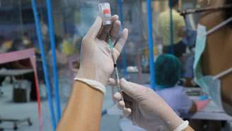 Mão segurando seringa e retirando líquido de frasco de vacina