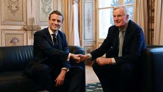 Macron (à esquerda) aperta a mão de Barnier, escolhido como o novo primeiro-ministro