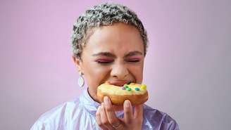 Mulher negra, de cabelos curtos e claros, mordendo um donut com cobertura amarela