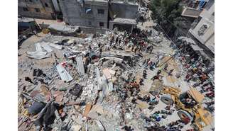 Palestinos se reúnem enquanto equipes de resgate procuram vítimas sob os escombros de uma casa atingida por um ataque israelense, em meio ao conflito entre Israel e o Hamas, no campo de refugiados de Nuseirat, no centro da Faixa de Gaza. 14/05/2024