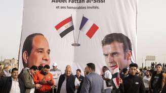 Egípcios caminham em frente a um banner de apoio ao presidente egípcio Abdel-Fattah el-Sissi, à esquerda, e seu homólogo francês Emmanuel Macron, durante a visita deles à cidade de Arish, no norte da Península do Sinai, cerca de 50 km (32 milhas) a oeste da fronteira com a Faixa de Gaza, Egito, terça-feira, 8 de abril de 2025. (Foto/AP/Mohamed Arafat)